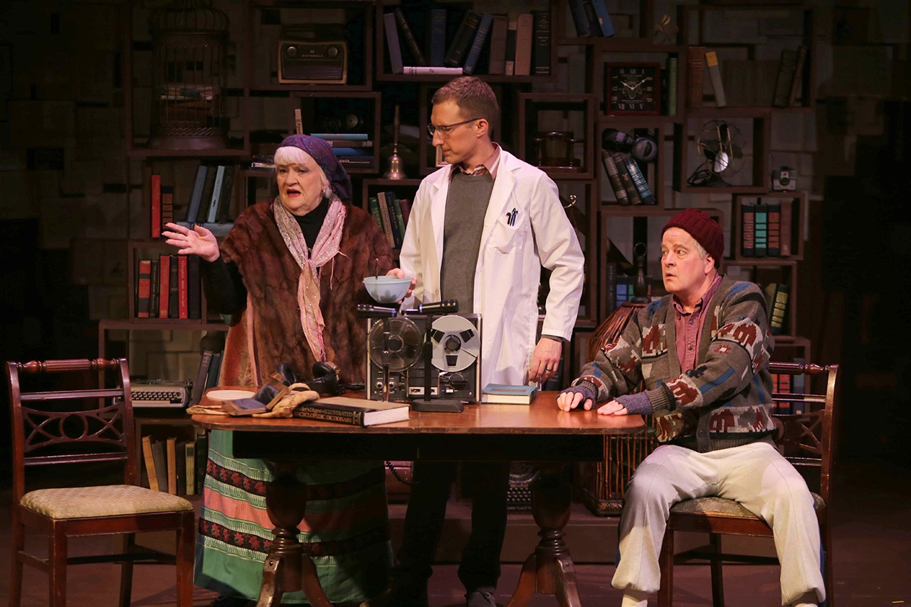 Alta (Louise Hoover) tries to get the linguistic scientist George (Ian Dorsch) to try some of her home-made stew, while her husband Resten (Keith Krueger) warns him against it in the Driftwood Players’ current production of “The Language Archive.” (Keith Krueger photo)