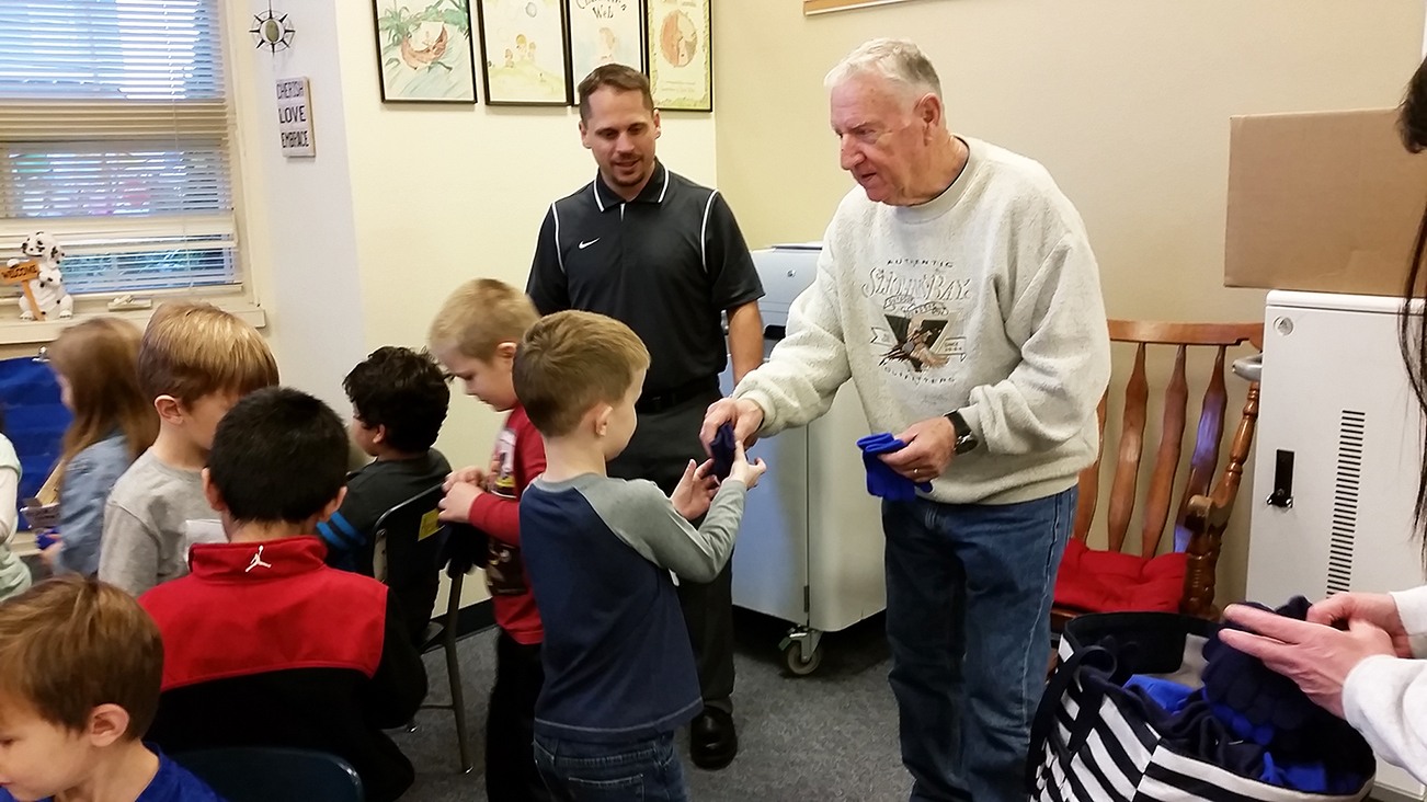 Joe Cornell of the nonprofit organization “Making a Difference for Grays Harbor Kids” hands a pair of gloves to a student Thursday at McDermoth Elementary School in Aberdeen as Principal Brandon Winkelman looks on. (Terri Harber|The Daily World)