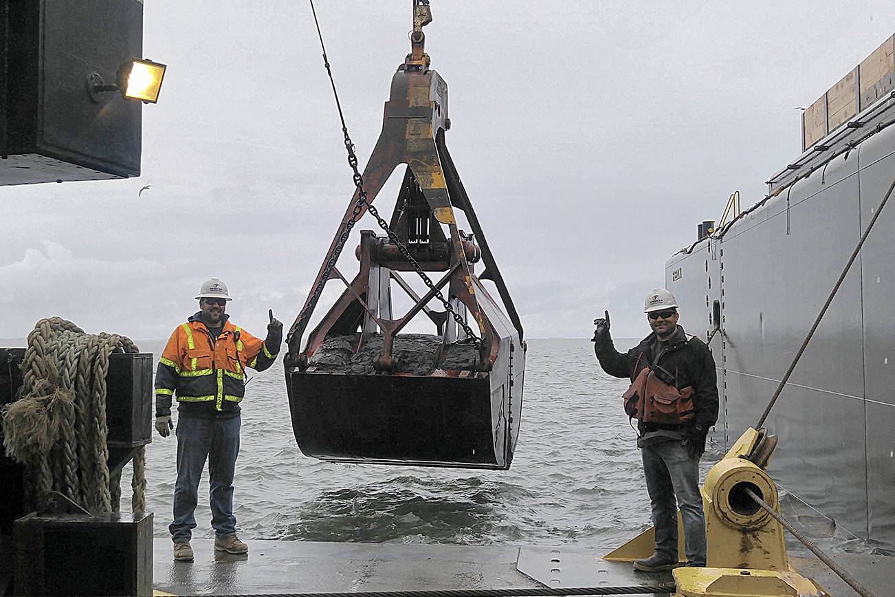 Army Corps of Engineers maintenance dredging of the outer harbor at Grays Harbor will begin April 1. Here Aaron McMahill and Chris Raymond from American Construction pose alongside the first bucket of dredged material taken from last year’s inner harbor dredging project.