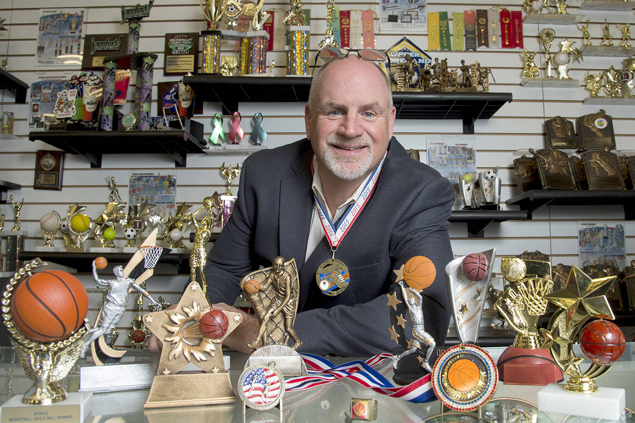 Keith Baldwin, 58, president of Spike&rsquo;s Trophies in Philadelphia, displays participation trophies on the counter. Baldwin himself participated in a triathlon recently and made a participation medal (like the one hanging around his neck) for himself. (Clem Murray/Philadelphia Inquirer)