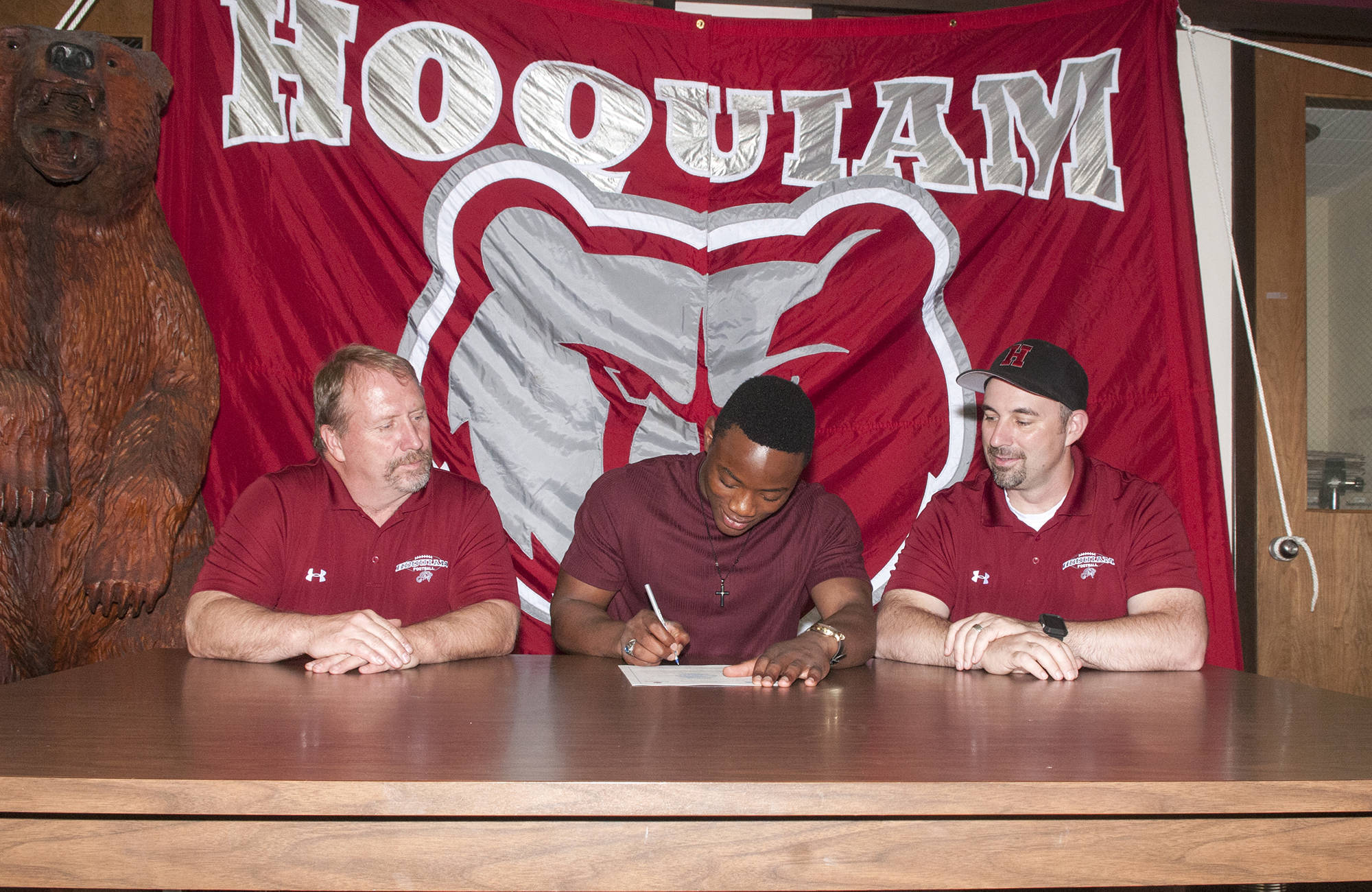(Brendan Carl | The Daily World) Hoquiam’s Artimus Johnson signs a letter of intent to play football at Linfield College as Grizzly coaches Rick Moore, left, and Jeremy McMillan watch on.