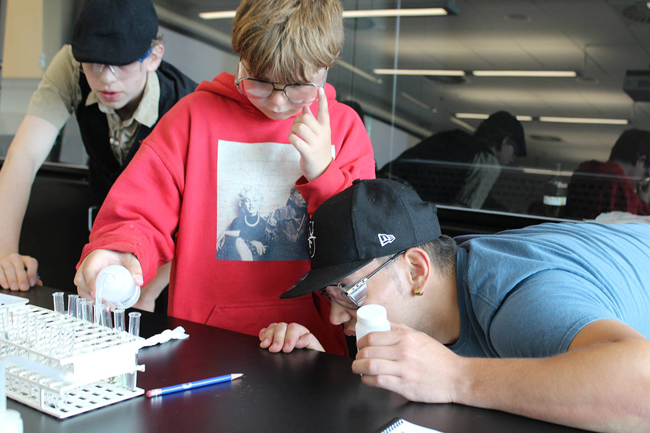 Stevens School sixth-grader Dyllan Hill, center, observes as his two Grays Harbor College lab partners, Joshua Latimer, left, and Andres Smiley study the solutions during a chemistry experiment on campus. (GHC photo)