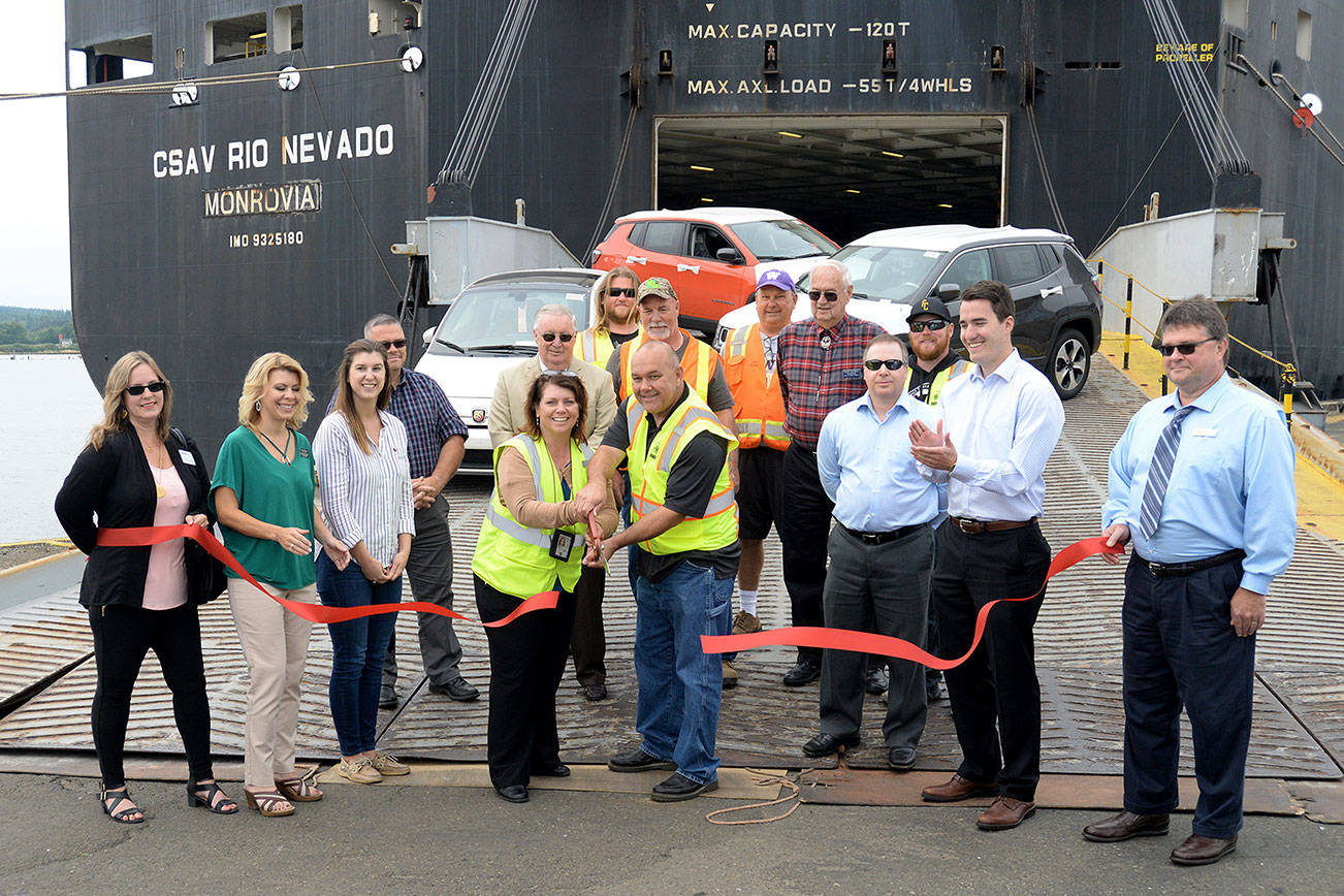 DAN HAMMOCK | THE DAILY WORLD                                The ribbon is cut as the vessel Rio Nevado unloads the first of what is expected to be 500 cars a month through a new agreement between Pasha Automotive and Chrysler. Holding the scissors at center are Pasha Port of Grays Harbor General Manager Penny Eubanks and Tim Ryker, Pasha’s Stevedoring and Terminals Operations Manager. From left are Loretta Thomas for WorkSource, Georgia Bravos from Jodesha Broadcasting, Rio Nevado Trade Manager Samantha Cibelli, Eubanks, Ryker, Greater Grays Harbor Inc. CEO Dru Garson, Hunter Larson and Eric Barre from the Aberdeen KeyBank branch. Behind Eubanks is Port Commissioner Stan Pinnick, behind Ryker is Mike Brown, a 40-year veteran of the Port and president of ILWU Local 24. To his left is Port Commissioner Chuck Caldwell.