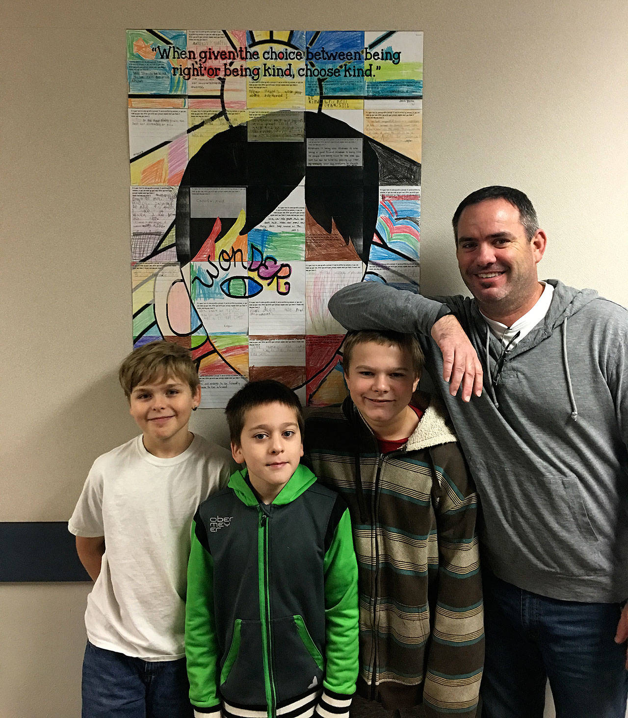 From left, Central Elementary students Eli Lavallee, Blake Anderson, James Young and teacher Chase Taylor stand in front of a student-made collage of what kindness means to them. The school in Hoquiam is participating in a month-long project to encourage students to conduct random acts of Kindness. (Courtesy Denise Pearl)