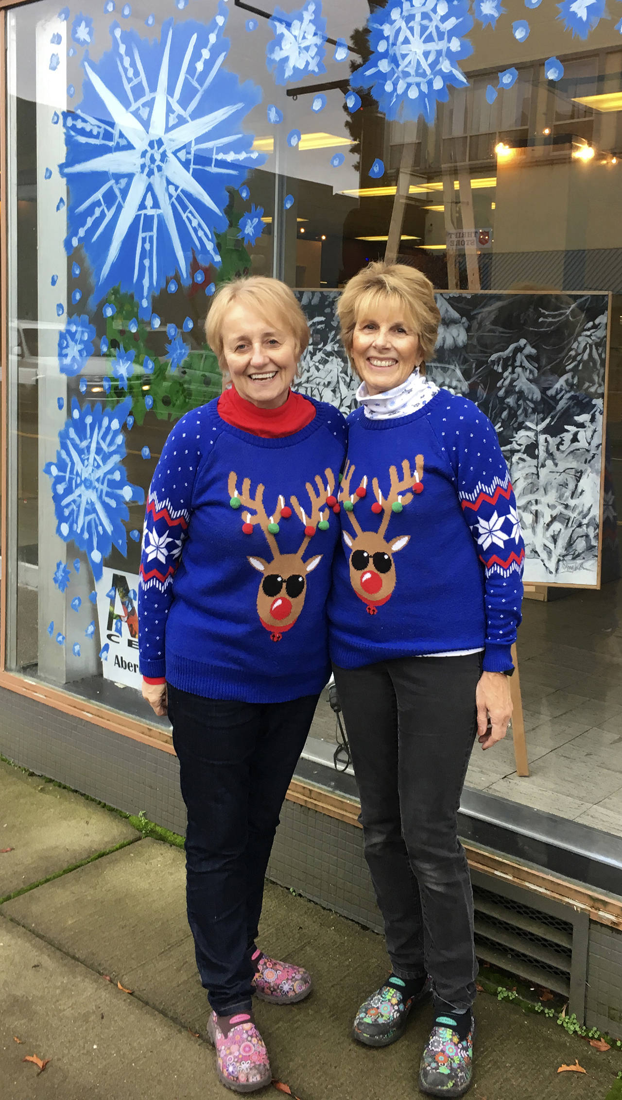 Kat Bryant | The Daily World                                Event co-organizers Bobbi McCracken, left, and Bette Worth stand outside the former site of Goldberg’s Furniture Store, where local artist Douglas Orr of the Aberdeen Art Center decorated the windows in preparation for the Winterfest Market.