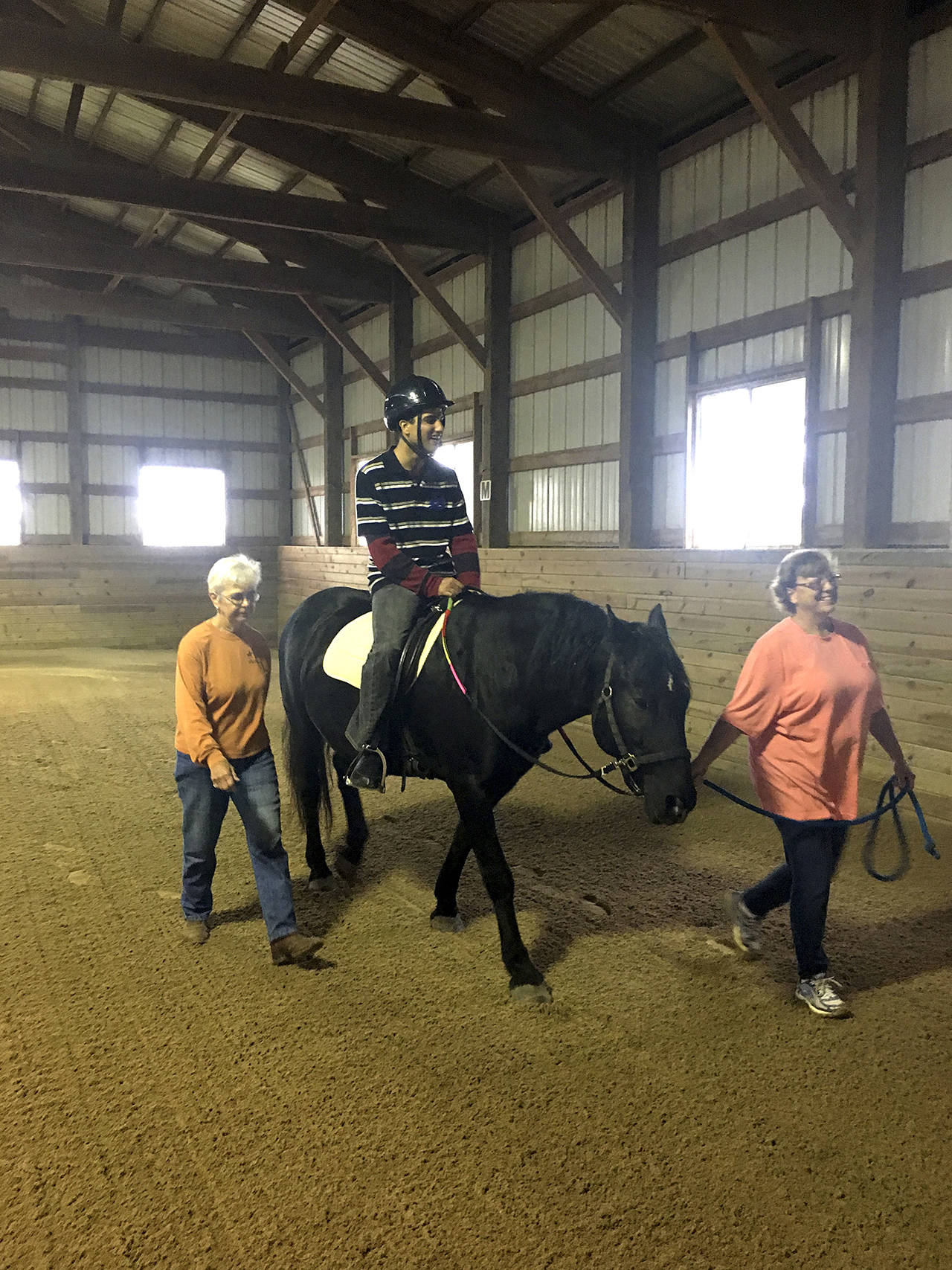 Cathy Janek | Chicago Tribune                                Volunteers Jan Lauwers and Liz Klemenswicz with Giant Steps help rider Waqas Kahn during a program at Rich Harvest Farms near Sugar Grove, Illinois.