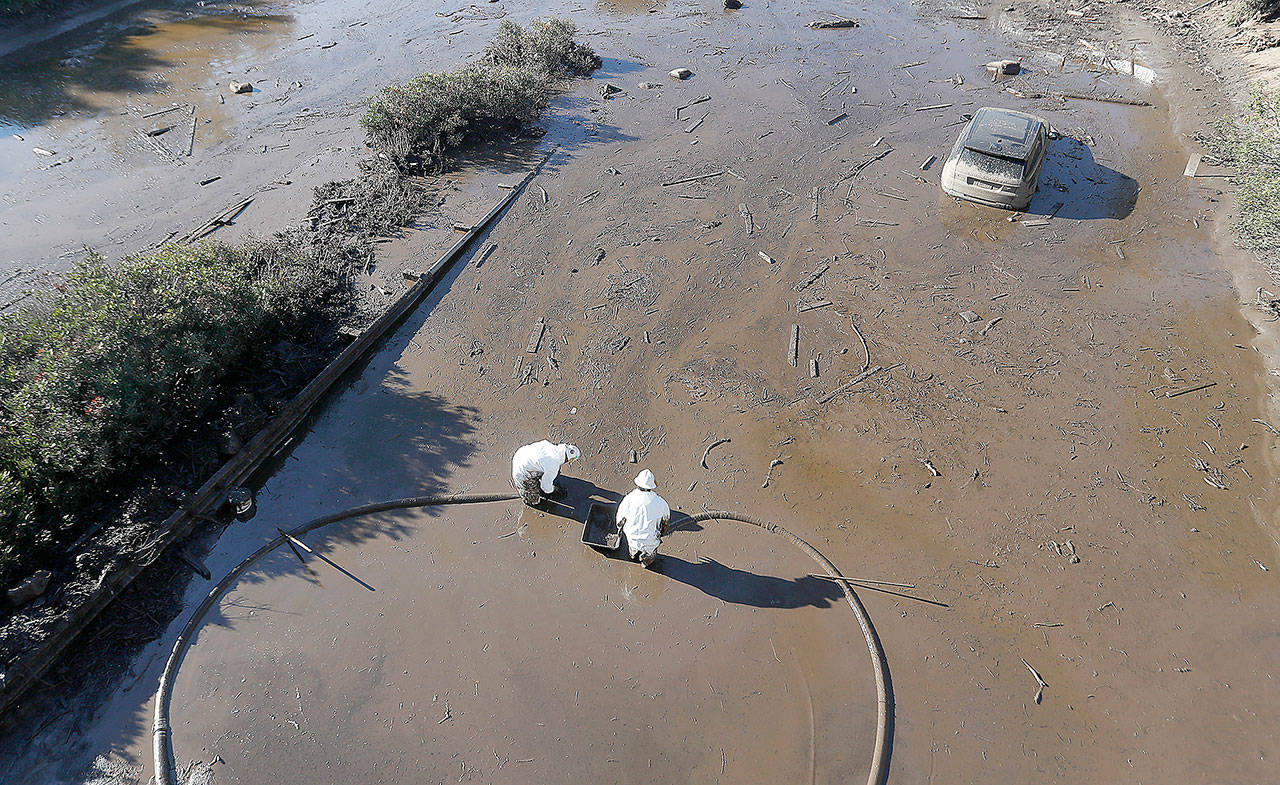 Workers are knee-deep in mud along a flooded stretch of U.S. Highway 101 in Montecito, Calif., on Saturday. (Luis Sinco/Los Angeles Times/TNS)