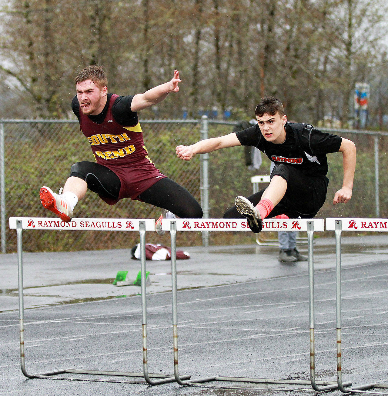 South Bend’s Ben Byington, left, and Raymond’s McCartney Maden battle over the hurdles Thursday during the Willapa Harbor tri-district meet. Maden won the race. (Photo by Larry Bale.)