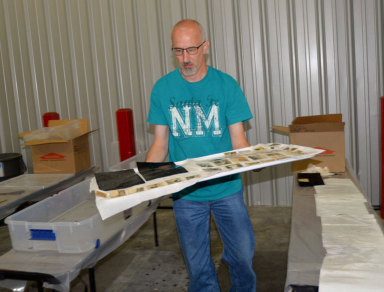 LOUIS KRAUSS | THE DAILY WORLD Volunteer Mark Vessey carries a tray of historic photos to a drying area after separating and cleaning them at a warehouse in Tumwater.