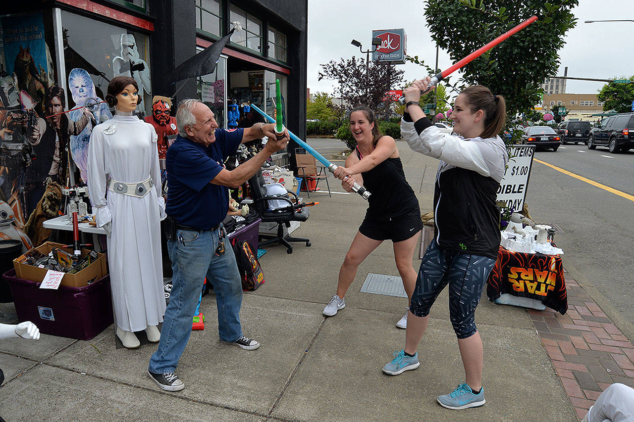 Louis Krauss | The Daily World                                Star Wars Shop owner Don Sucher, left, and customers Johanna and Vanessa Brulotte practice for the Space Force with plastic lightsabers.