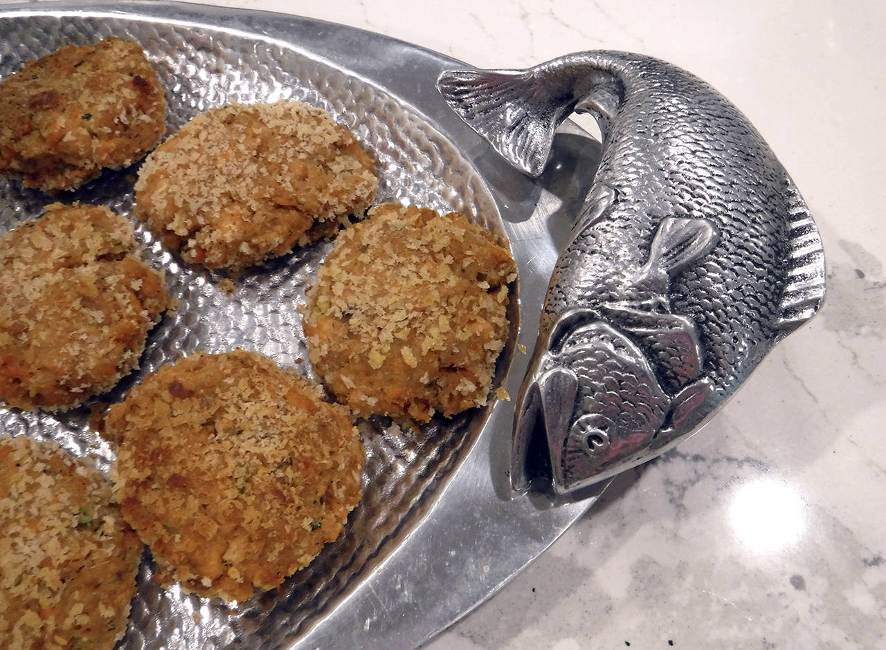 (Mitchell Chapman) Salmon cakes served on a textured Bruce Fox Designs oval tray with two salmon sculpture handles.