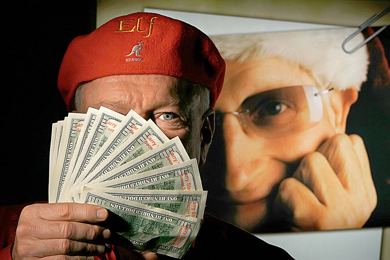 In the Christmases after the loss of Larry Stewart, pictured in background, a new legion of “Secret Santas,” including this Kansas City area man, continue in Stewart’s legacy of handing out cash to unsuspecting area residents. The $100 bills are stamped with the words “Larry Stewart Secret Santa.” (David Eulitt/Kansas City Star)