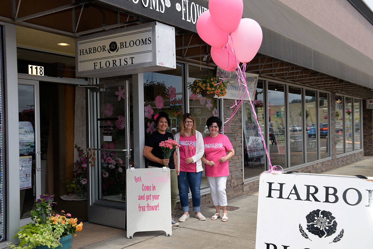 (Louis Krauss | Grays Harbor News Group) Angela Johnson, left, Sheril Woodruff and Sharon Poor stand outside Harbor Blooms in Aberdeen, holding up pink carnations they were giving out Friday as part of Bloom Day.