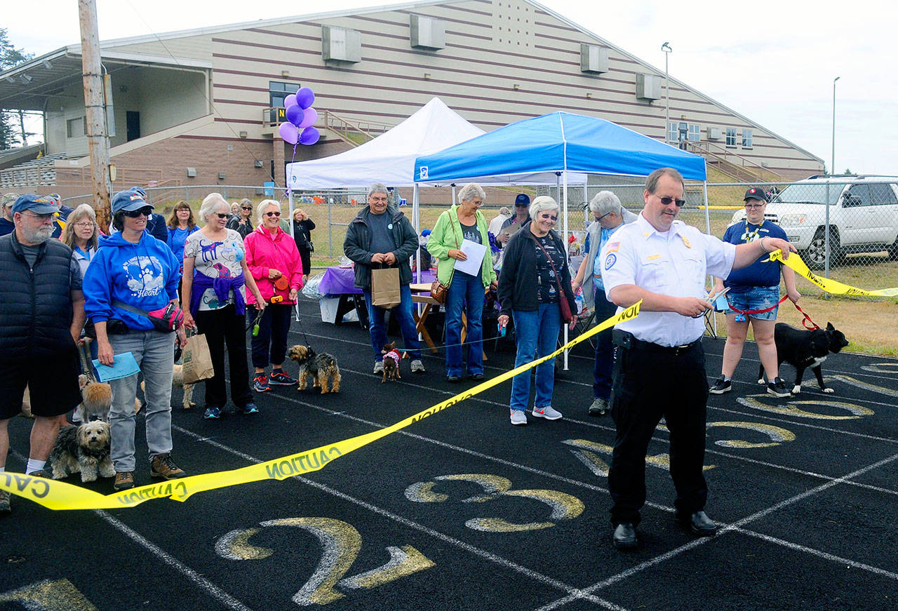 Hasani Grayson | Grays Harbor News Group                                Ocean Shores Fire Chief Mike Thuirer cuts the police tape ribbon to signal the start of the Woof-a-Thon walk around the track at North Beach High School on Saturday.