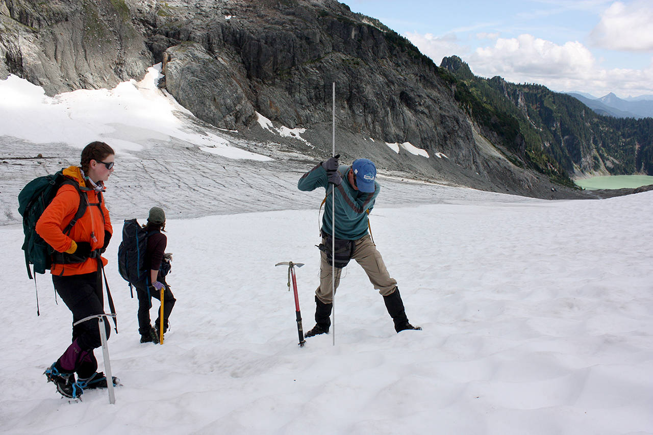 Researcher Ann Hill watches Mauri Pelto jam a metal pole into the snow to measure how deep it is. If it’s less than 8 feet deep it won’t last the summer. (Zachariah Bryan / The Herald)