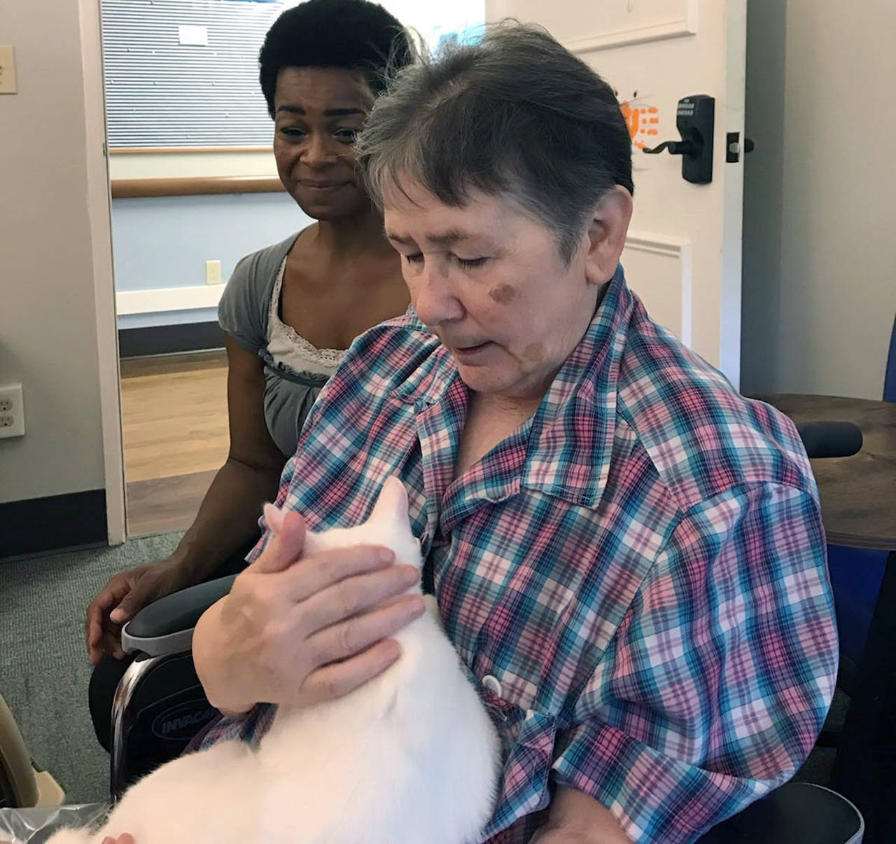 Courtesy photo                                Grays Harbor PAWS volunteer Amy Bates kneels next to Pacific Care resident Frannie Brown as she cuddles with Spot, one of the Aberdeen shelter’s adoptable cats. Bates visits the Hoquiam facility every Tuesday with a few PAWS residents in tow. “The residents look forward to her coming,” said Shannon Ashlock, activity director at Pacific Care.