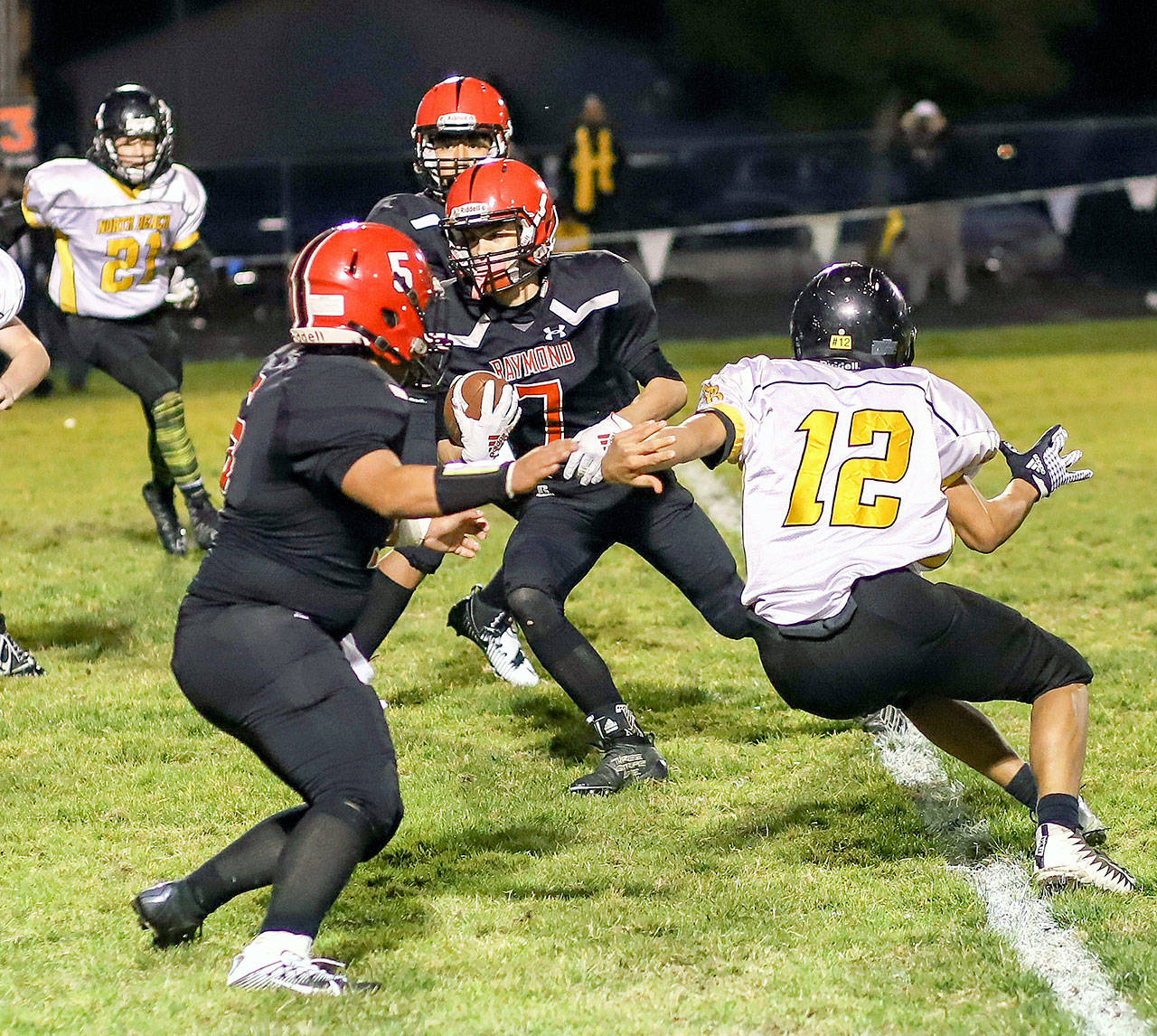 Raymond’s McCartney Maden (7) finds an opening on the way to his first rushing touchdown while Jose Delgado (5) creates an opening with a block on North Beach’s Josh Bighead (12) during Friday’s game in Raymond. (Photo by Larry Bale)
