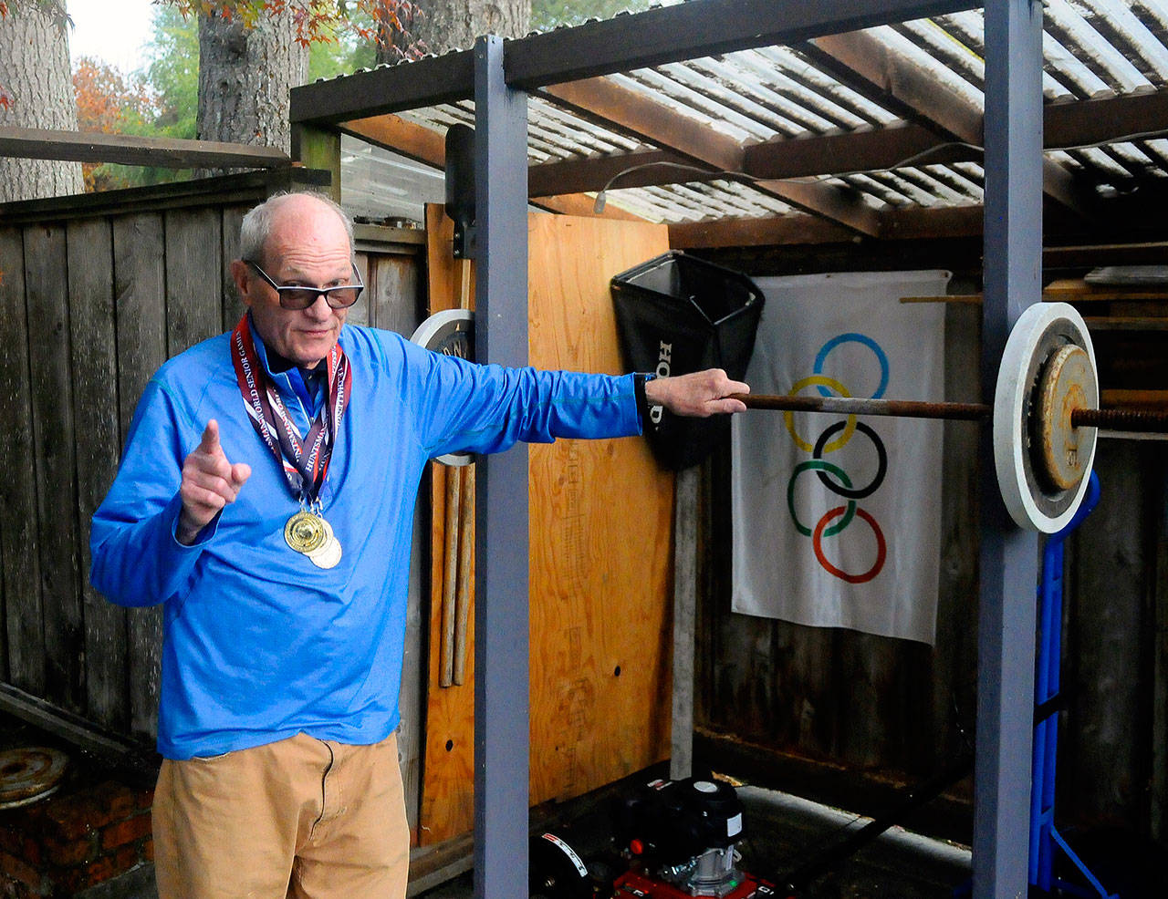 Paul Roberts stands next to his homemade squat rack in his backyard while wearing the medals he earned at the World Senior Games earlier this year. (Hasani Grayson | Grays Harbor News Group)