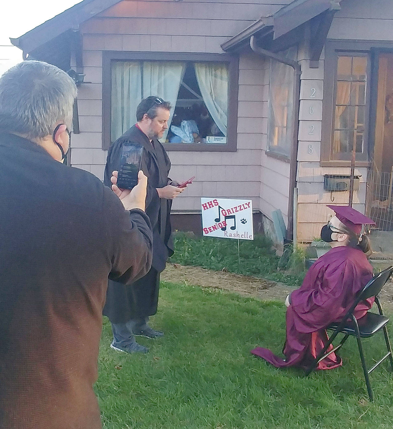 Lin Messerer photo                                Hoquiam High School Principal Brock Maxwell conducts a mini graduation ceremony for senior Rashelle Bates on her front lawn as her mother, Rhea Abbott, watches from her bed inside.