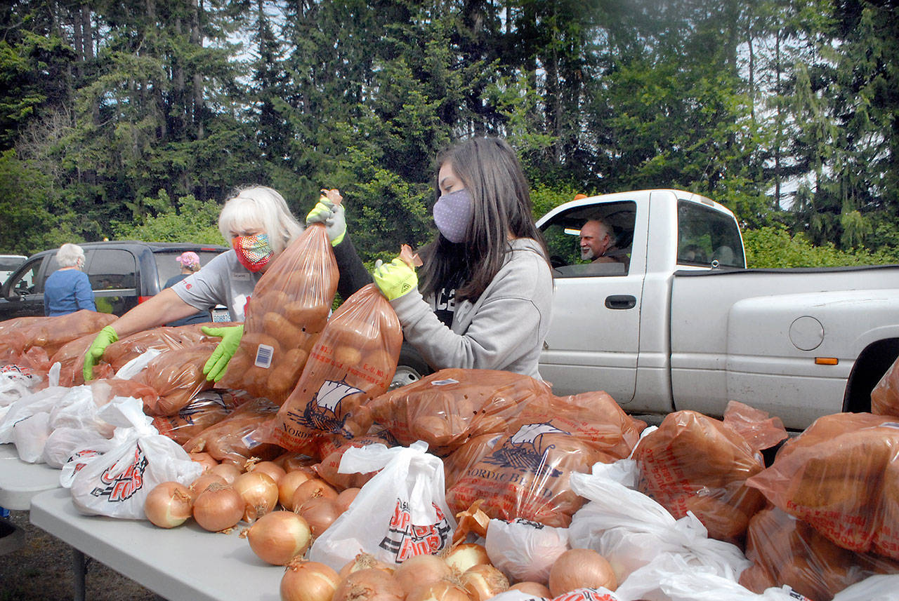 Keith Thorpe/Peninsula Daily News                                 Volunteers Delores Hampton, left, and Tavita Bucio, both of Sequim, pick up bags of potatoes and onions for placement into a waiting vehicle during a giveaway at the Clallam County Fairgrounds in Port Angeles in May. The organizer of that giveaway, Connie Beauvais, has announced four locations for a similar event, all potatoes, in Grays Harbor County starting Friday.