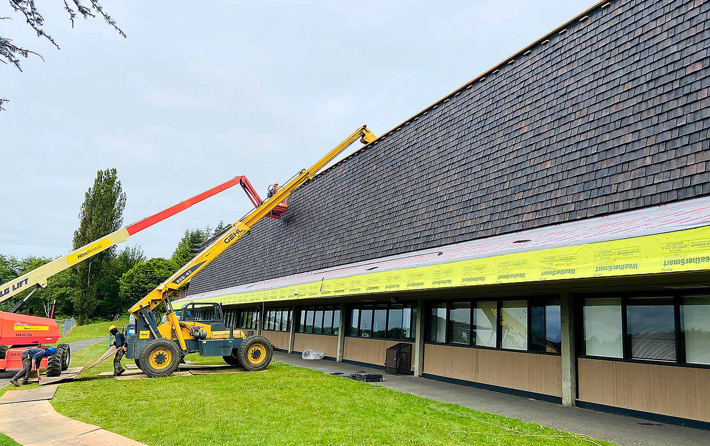 COURTESY PHOTO                                 Replacement of the old cedar shakes at Hoquiam High School is underway. Here you can see the new composite shakes going up, which match the look of the Mansard-style roof and will hold up to Hoquiam weather.