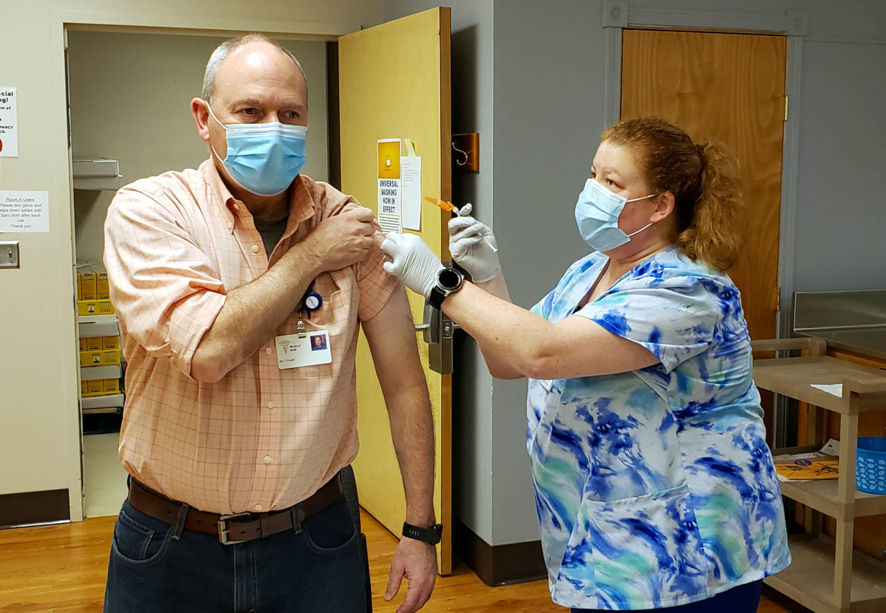 Dr. Tim Troeh, left, receives a COVID-19 vaccination from nurse Jeannine Roth on Tuesday at Grays Harbor Community Hospital in Aberdeen. (Ryan Sparks | The Daily World)