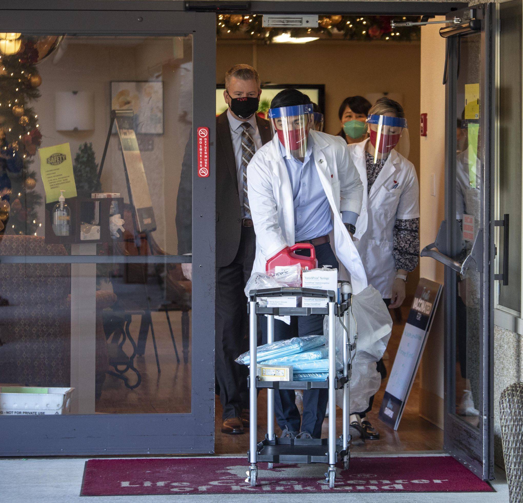 Steve Ringman / Seattle Times
Matt Talavera, a pharmacist for CVS, wheels a cart out of the Life Care Center in Kirkland, where he started giving the vaccine to employees of the Center on Monday.