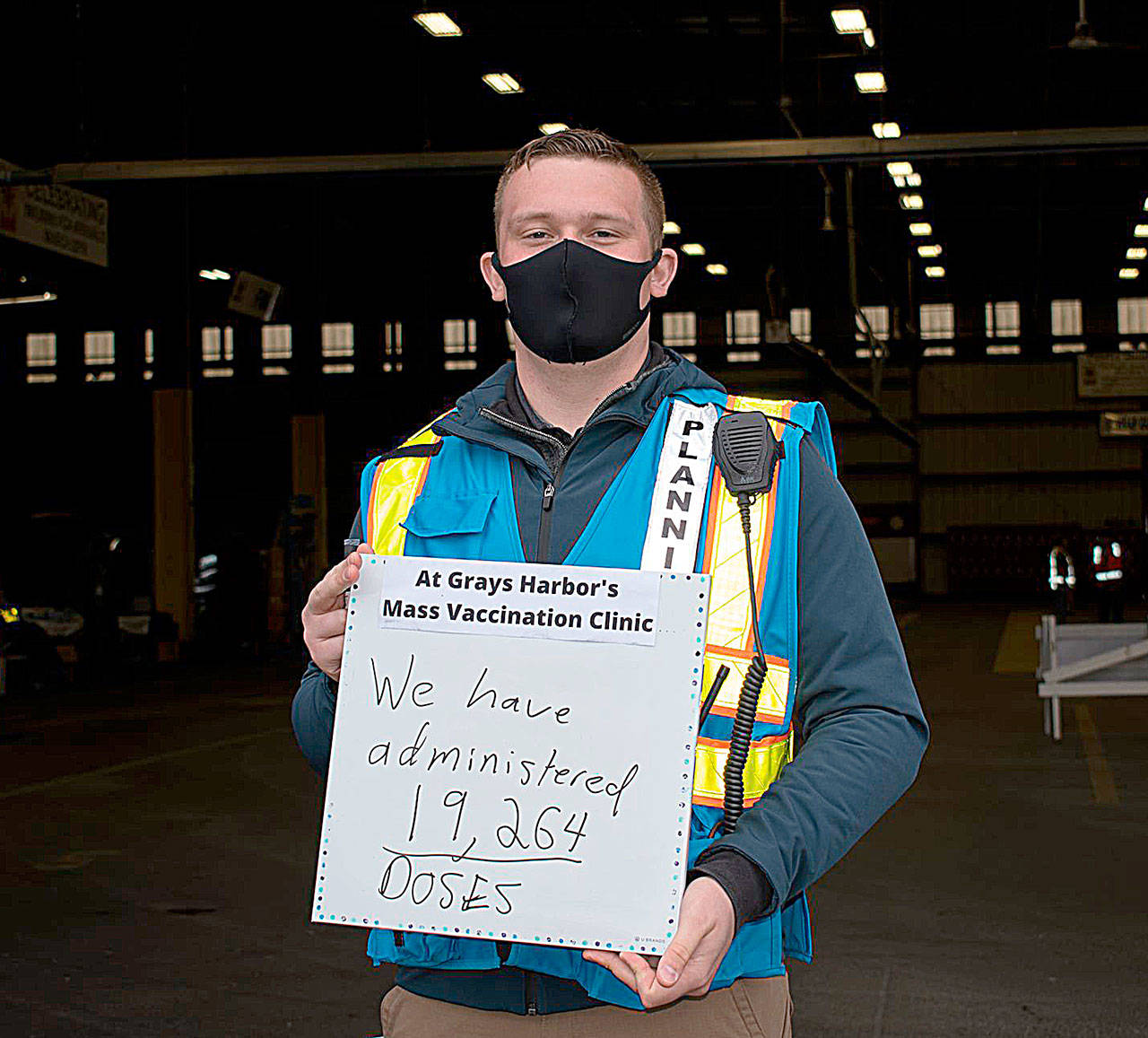 NIKKI GWIN PHOTO 
Grays Harbor County COVID-19 Incident Management Team Planning Section Chief Nick Falley holds a sign showing the total number of shots administered at the mass vaccination site at the Port of Grays Harbor. The last day of operations at the site was Friday.