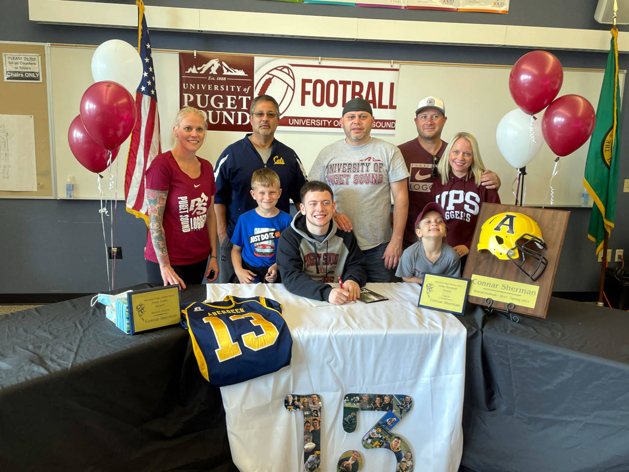 SUBMITTED PHOTO Aberdeen senior Connar Sherman, sitting, is surrounded by family members after signing a National Letter of Intent on Wednesday to play football for the University of Puget Sound in the fall. Pictured are (from left) step-mother Racquel Sherman, Aberdeen assistant coach John Bowers, brother Camden Mayr (blue shirt), father Henry Sherman, step father Josh Mayr, mother Sarah Mayr and sister Shyla Mayr.