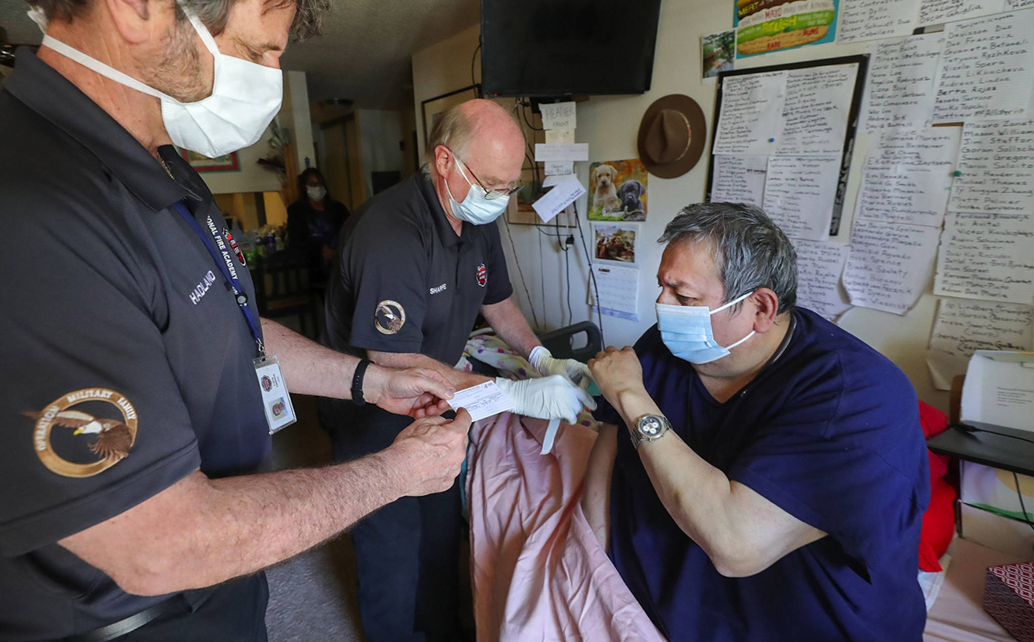 South County Fire paramedic Larry Hadland, left, hands a proof of vaccination card while emergency medical technician Kim Sharpe vaccinates Abel Cordova, 63, at his home on April 20, 2021. Cordova was unable to travel for a vaccination. Greg Gilbert |The Seattle Times