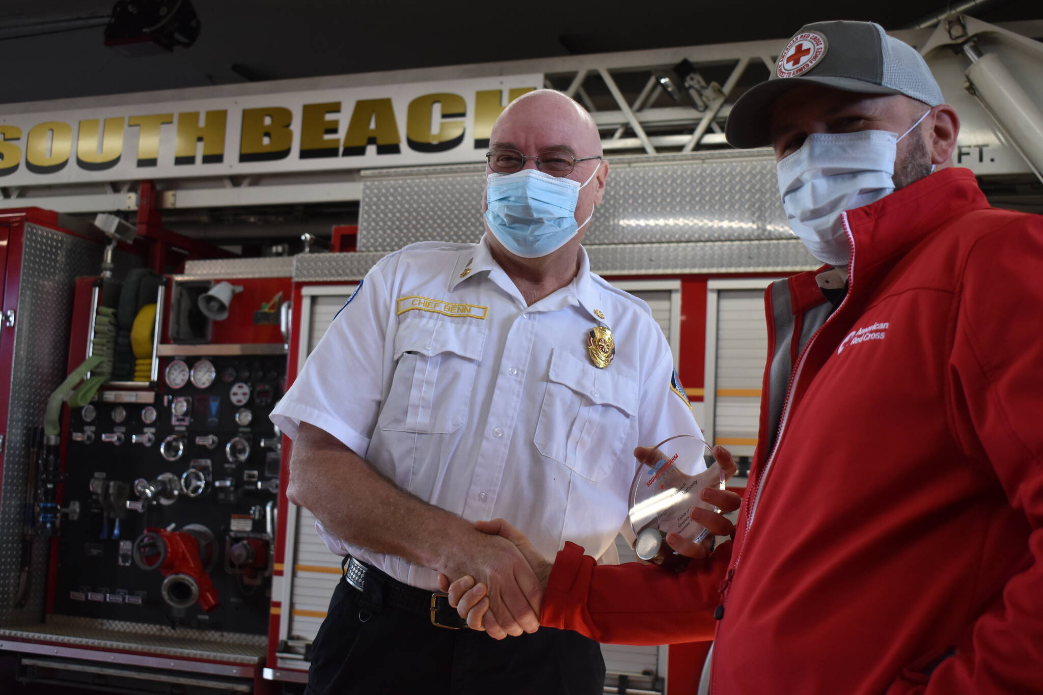 Matthew N. Wells | The Daily World 
Dennis Benn, fire chief at South Beach Regional Fire Authority, left, shakes hands with Dan Wirth, executive director of American Red Cross South Puget Sound and Olympics Chapter, after Wirth helped present Benn and his crew an award on Friday, Feb. 11, 2022, for saving the life of a family in Grayland through a joint campaign to ensure homes have working smoke alarms.