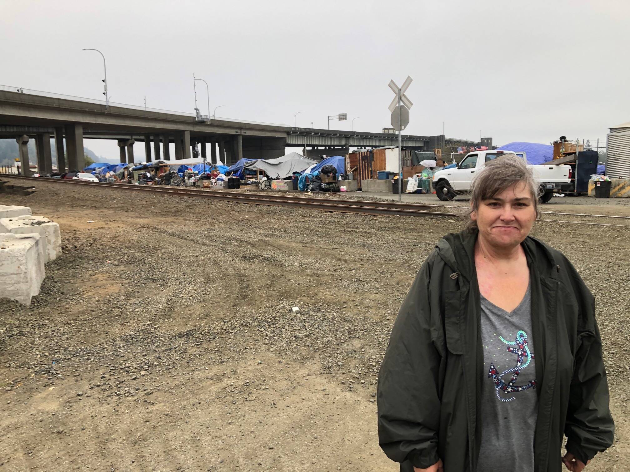 Joyceanne Collins stands in front of a homeless camp at the base of the Chehalis River Bridge along the railroad tracks on Monday.