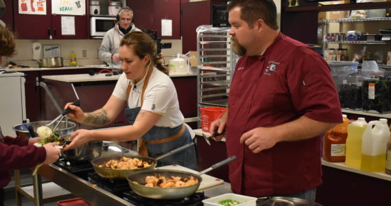 Allen Leister | The Daily World
Chef Elise Landry (left) and Rob Paylor (right) serve a line of hungry students a plate of shrimp and grits over rice with a side of salad that was prepared live by Landry. Paylor said his experience at Landry’s restaurant, Chicory, motivated him to invite Landry to demonstrate her cooking skills to the class.