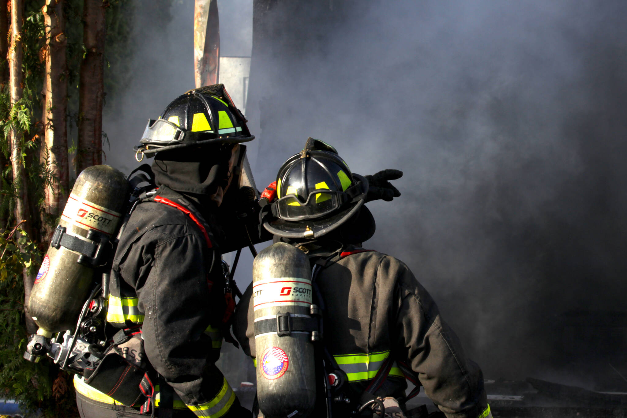 A firefighter points something out to their colleague as they attack a structure fire in Elma on Nov. 15. (Michael S. Lockett / The Daily World)