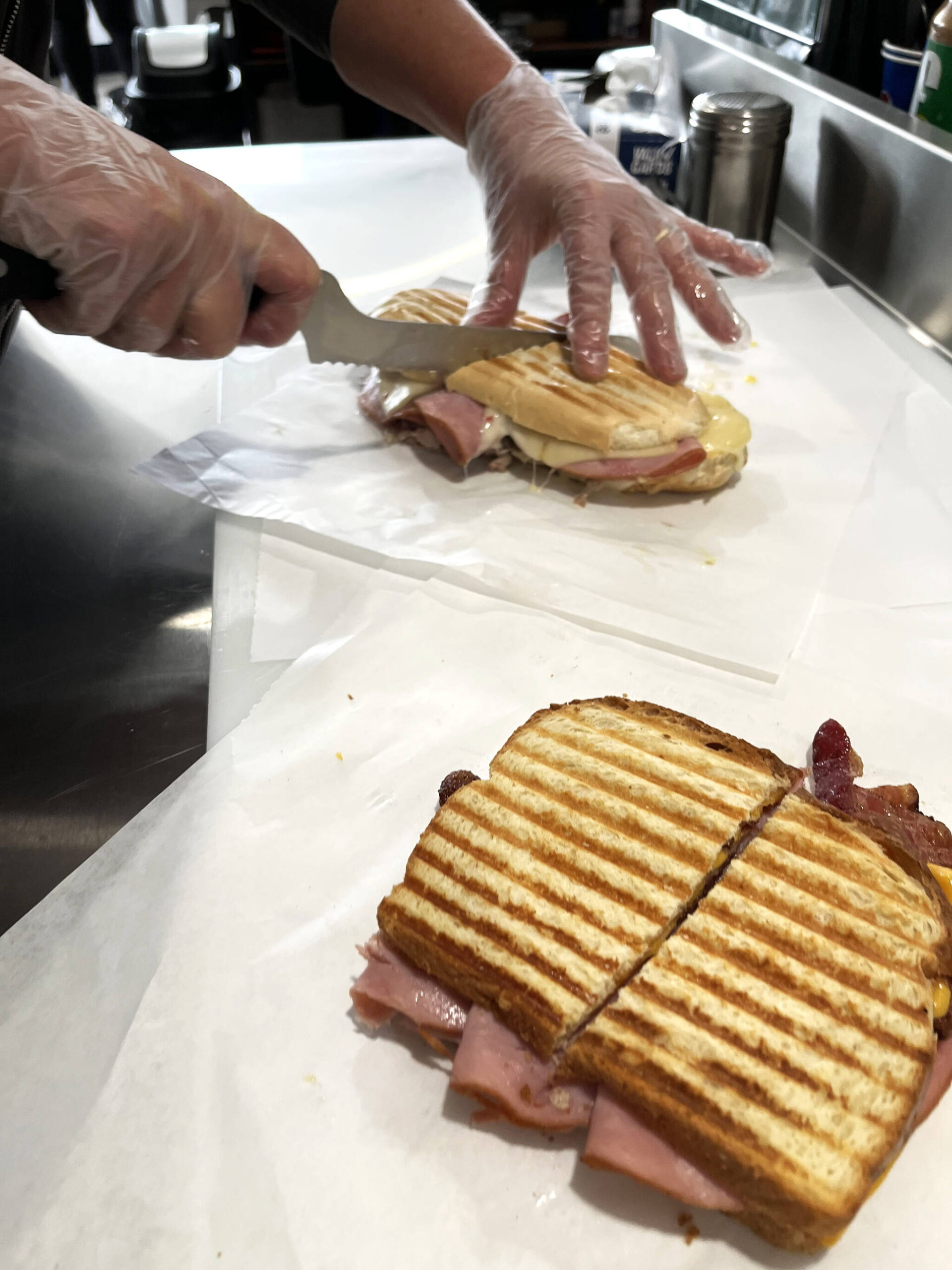 Shelly Dixon, after pulling off a freshly-grilled breakfast sandwich from the press, cuts into The Cuban sandwich, which comes with six ounces of pulled pork.