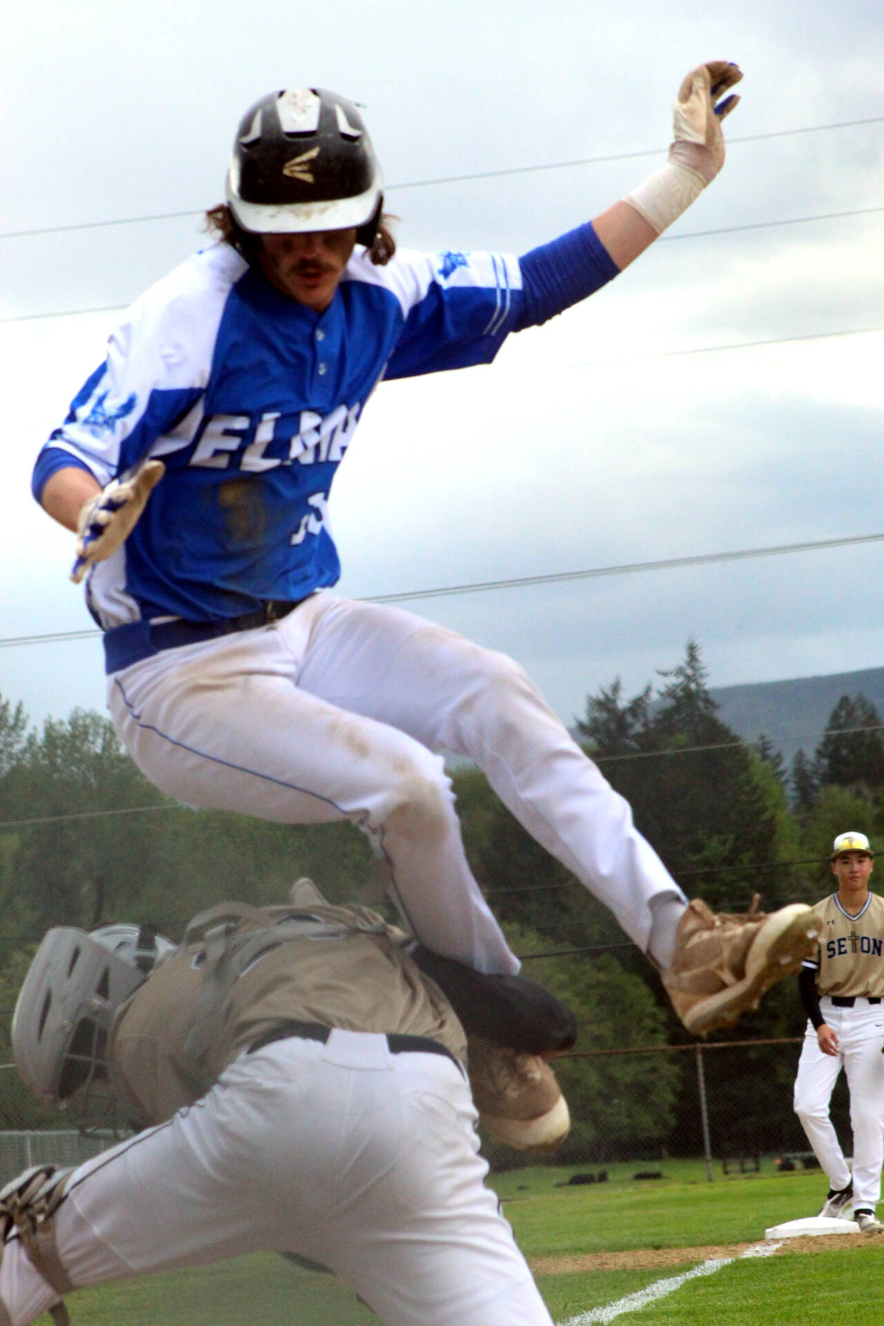 PHOTO BY TATUM SANDERS Elma’s Gibson Cain leaps over Seton Catholic catcher Ryker Ruelas to score a run during the Eagles’ 7-2 win in a 1A District 4 first-round game on Monday at Castle Rock High School.