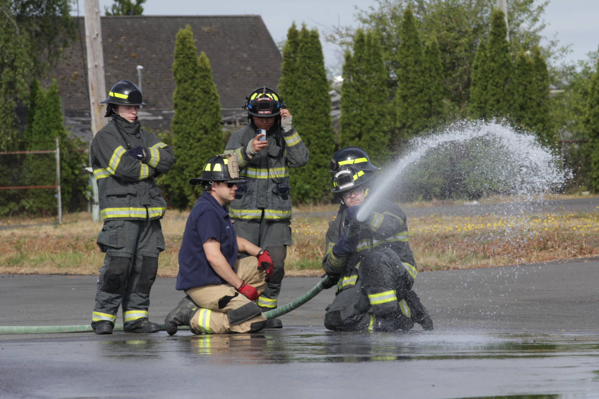 Derek Jensen of the Hoquiam Fire Department, in blue T-shirt, teaches a group of high schoolers taking part in a fire science program about using a firehose on July 13. (Michael S. Lockett / The Daily World)
