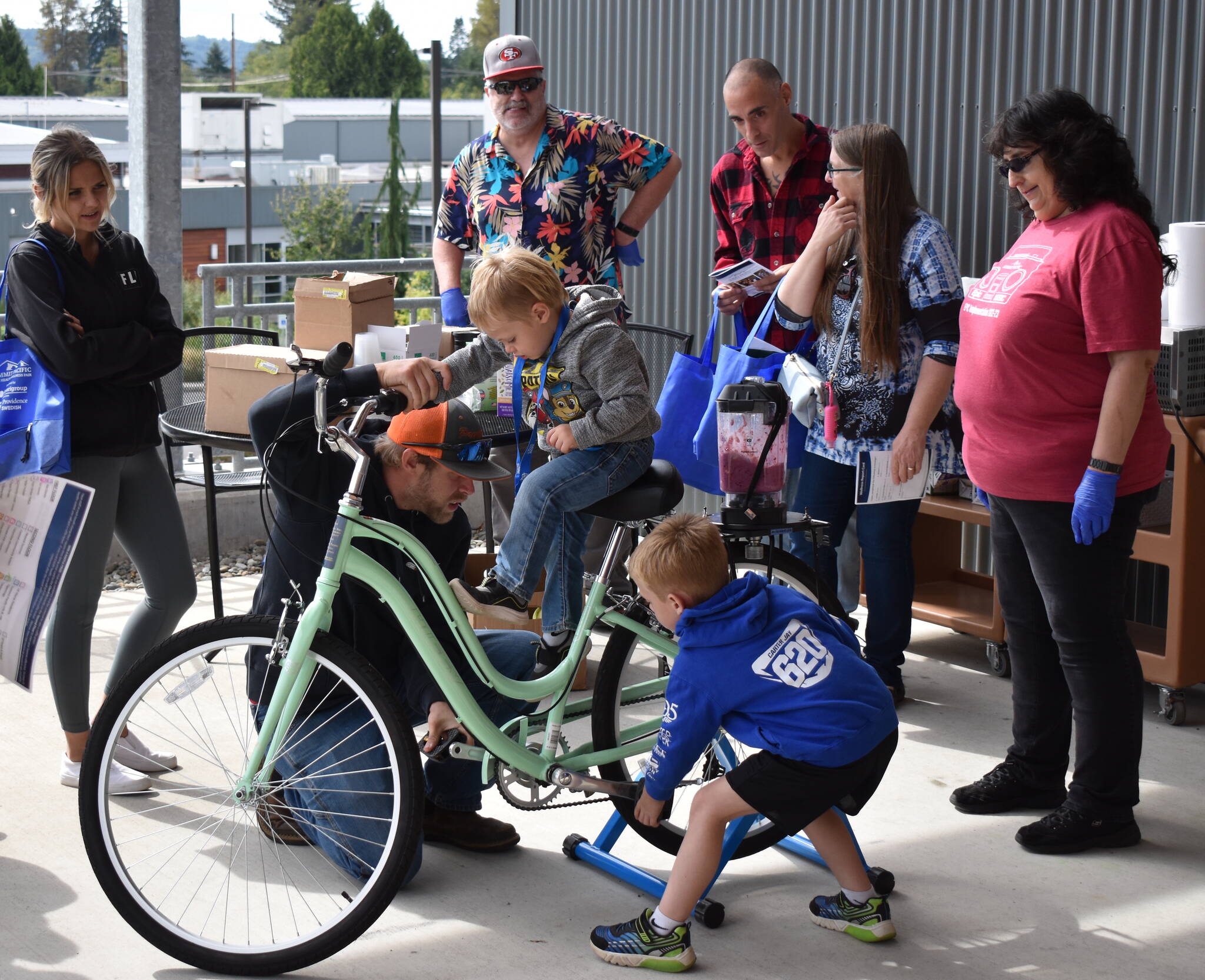 Wellness fair attendees ride a blender-powering bicycle at the 2022 Summit Pacific Peak Health and Wellness Fair. (Allen Leister / The Daily World File)
