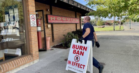 Hoquiam fire Capt. Brandon Ray carries in a burn ban sign as the county eases restrictions with the advent of cooler, damper fall weather on September 19. (Michael S. Lockett / The Daily World)