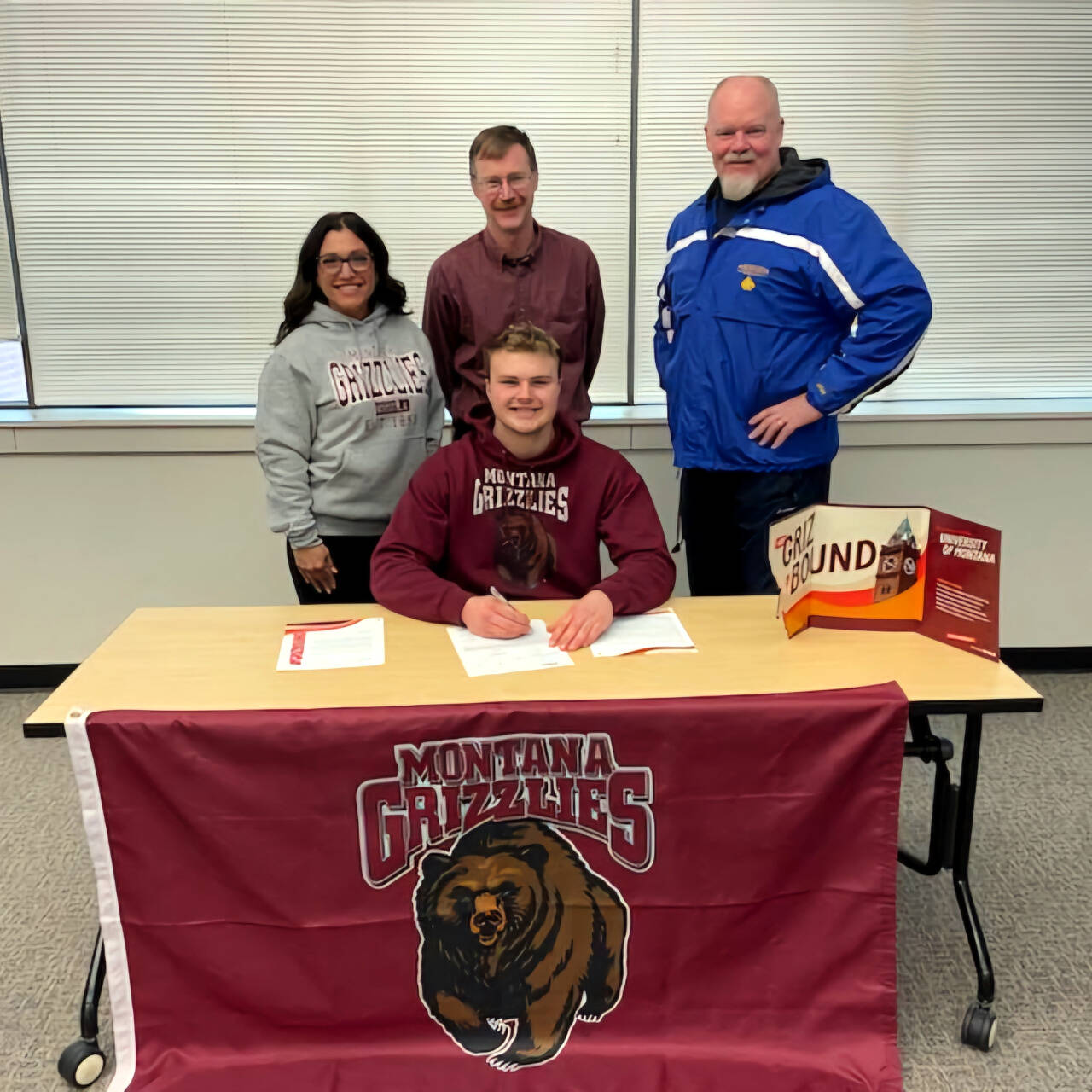 SUBMITTED PHOTO Aberdeen High School track and field star Tyler Bates, sitting, is surrounded by (from left) Bobcats head coach Desiree Glanz, father Todd Bates, and Aberdeen throwing coach Todd Bridge after signing a National Letter of Intent to attend the University of Montana in the fall on Wednesday in Aberdeen.