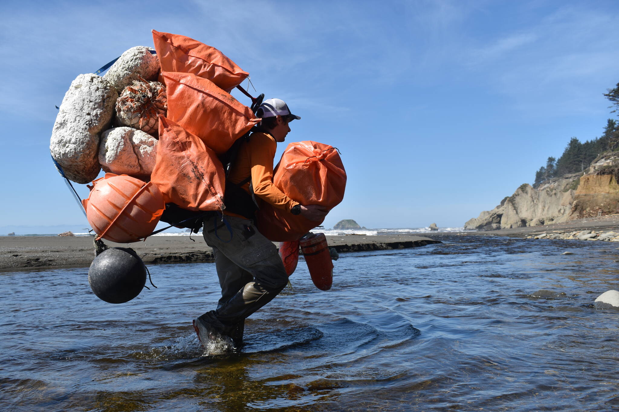 Kyle Deerkop, farm operations manager with Pacific Shellfish, crosses a creek hauling pounds of marine debris collected from a beach on the Quinault Indian Reservation. (Clayton Franke / The Daily World)