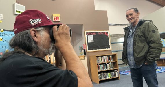 Clayton Franke / The Daily World
Ken Stevens, a Quinault tribal elder and former Taholah School Board member, peers into a virtual reality headset at the Taholah School Library on April 6 as Bill Adams, current school board member, looks on. As part of an open house to get ideas for the new planned Taholah school, the headset gave Stevens a virtual tour of the recently-constructed Toledo High School, which was designed by the same firm the district hired in Taholah.