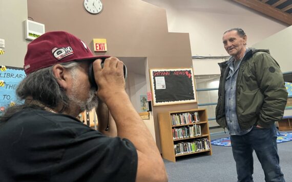 Clayton Franke / The Daily World
Ken Stevens, a Quinault tribal elder and former Taholah School Board member, peers into a virtual reality headset at the Taholah School Library on April 6 as Bill Adams, current school board member, looks on. As part of an open house to get ideas for the new planned Taholah school, the headset gave Stevens a virtual tour of the recently-constructed Toledo High School, which was designed by the same firm the district hired in Taholah.