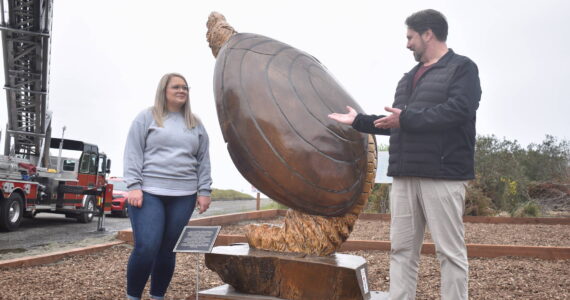 Clayton Franke / The Daily World
Ocean Shores City Clerk Sara Logan, left, and City Administrator Scott Andersen unveil Anthony Robinson’s giant razor clam statue near the Chance A La Mer beach entrance on Wednesday, April 24.