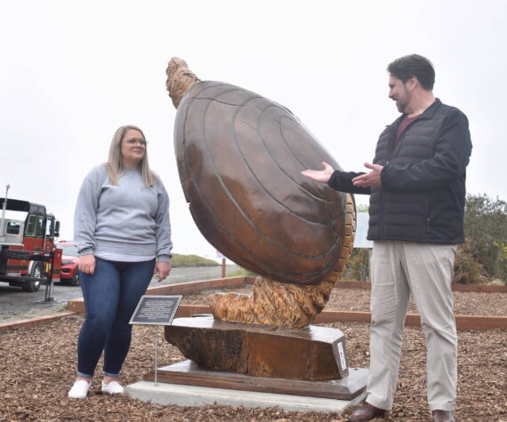 Clayton Franke / The Daily World
Ocean Shores City Clerk Sara Logan, left, and City Administrator Scott Andersen unveil Anthony Robinson’s giant razor clam statue near the Chance A La Mer beach entrance on Wednesday, April 24.