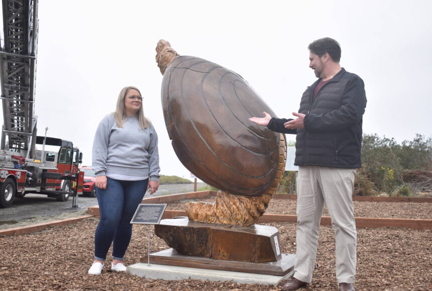 <p>Clayton Franke / The Daily World</p>
                                <p>Ocean Shores City Clerk Sara Logan, left, and City Administrator Scott Andersen unveil Anthony Robinson’s giant razor clam statue near the Chance A La Mer beach entrance on Wednesday, April 24.</p>