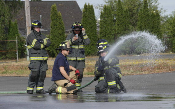 Michael S. Lockett / The Daily World
Derek Jensen of the Hoquiam Fire Department, in blue T-shirt, teaches a group of high schoolers taking part in a fire science program about using a firehose in 2023.
