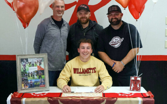 PHOTO BY LARRY BALE Raymond senior Austin Snodgrass (sitting) signed a Letter of Intent to compete in both football and track and field at Willamette University in the fall. Pictured with Snodgrass is (from left) Raymond athletic director Mike Tully and coaches Ken Minks and Luke Abbott.