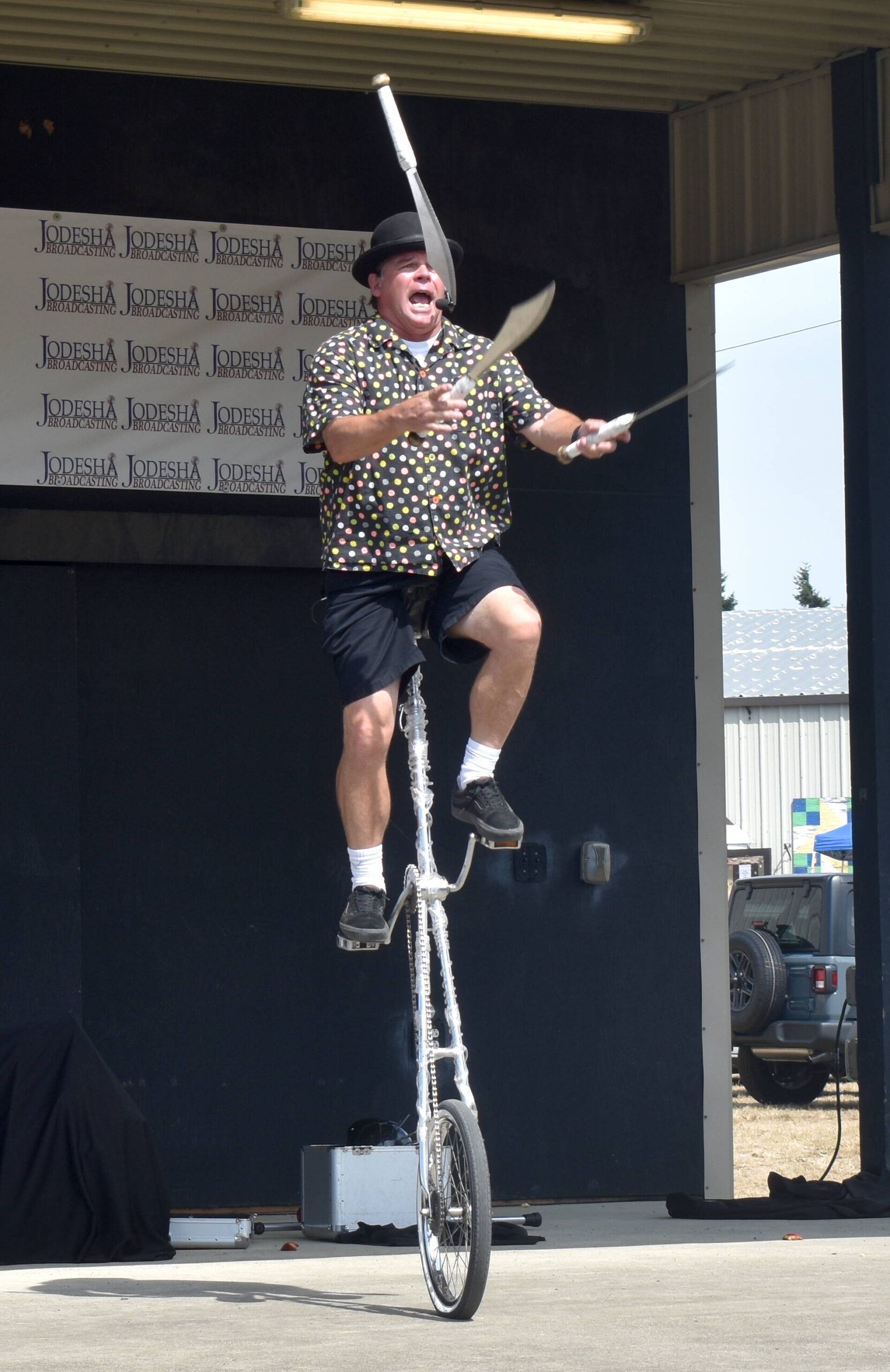 Roberto the Magnificent juggles while riding a unicycle.