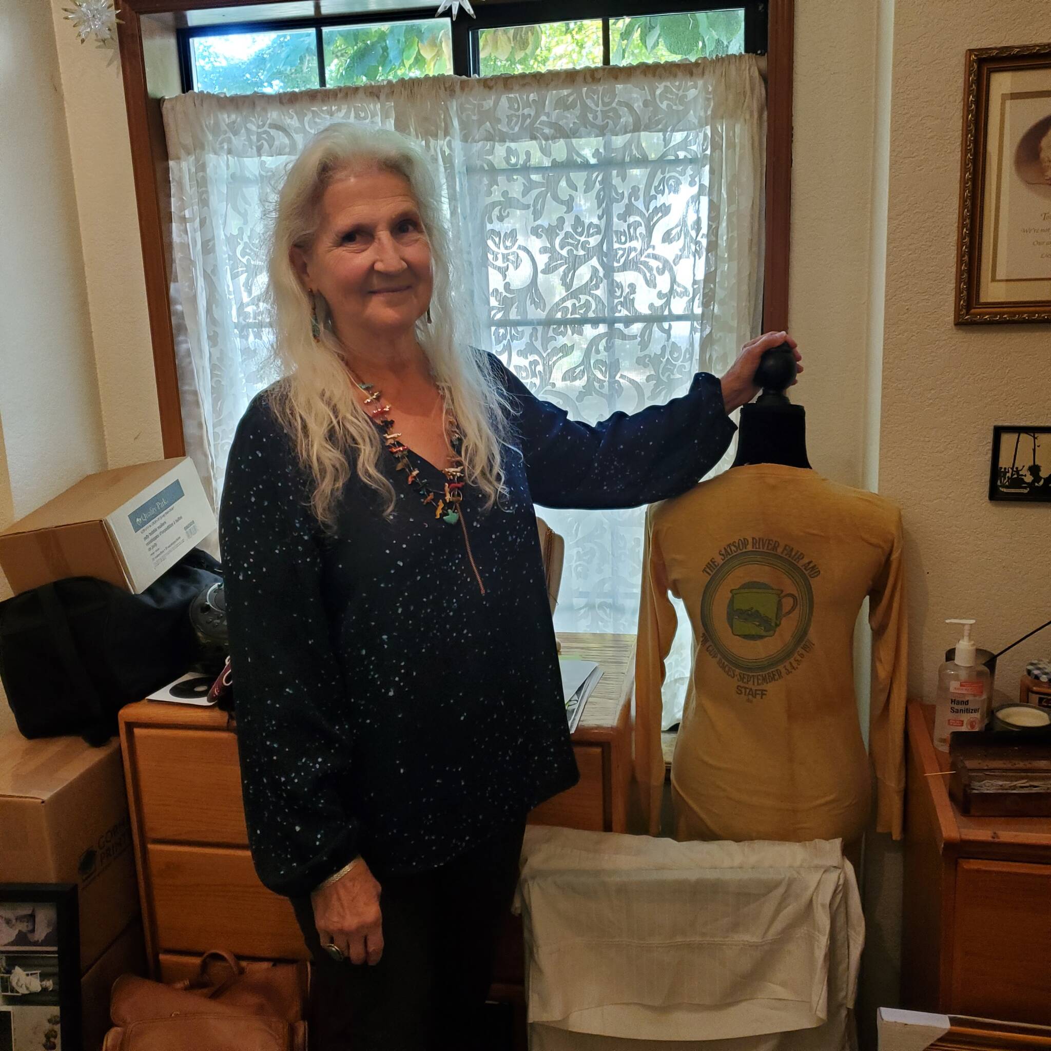 Andrea Watts / The Daily World
Leann Paul poses next to the shirts that staff of the 1971 Satsop Rock Festival wore. Paul was one of the owners of the property where the 1971 Satsop Rock Festival was located. Of her experience being on the stage and looking out on the crowd of people, “They looked like a beautiful swirling exotic cocktail of people, and the cloud of energy rising off them was tangible, I thought, so this is what a rock festival is all about.”